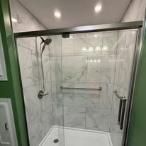 A tiled shower with a glass door, grab bar, and handheld showerhead.