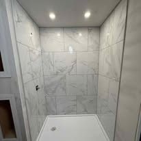 White tiled shower stall with a white rectangular base, lit by recessed ceiling lights.