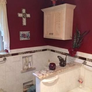 Bathroom with white tile, red walls, and a small cabinet. A cross and decorative items are displayed.