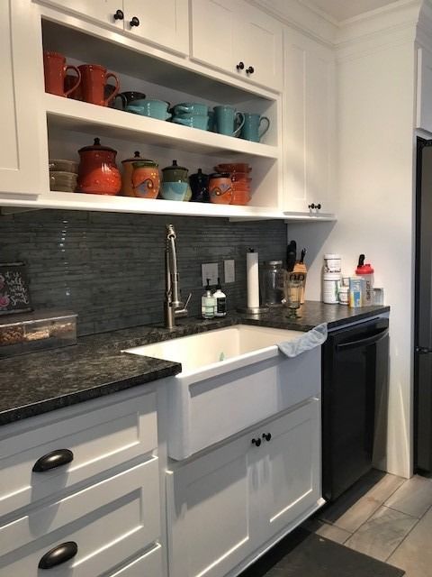 White kitchen cabinets with open shelves holding colorful mugs and jars; a farmhouse sink.