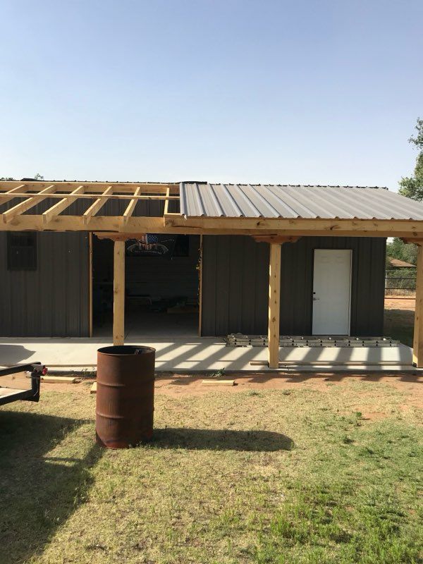 A partially constructed gray metal-sided building with a wooden porch under a blue sky.