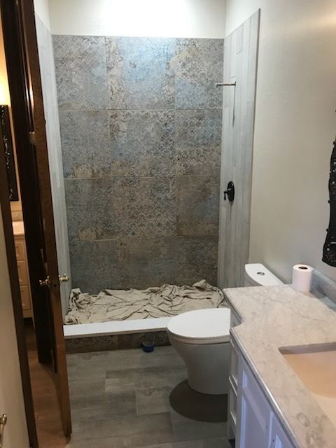 Bathroom with tile shower, toilet, and vanity. Gray, blue, and brown tiles. Beige floor. White cabinets and countertop.