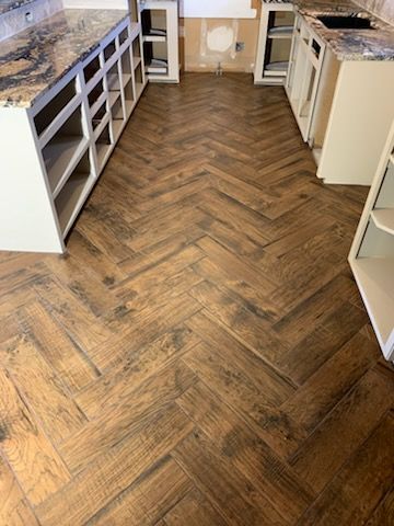 Herringbone wood floor in a kitchen under construction with white cabinets and granite countertops.