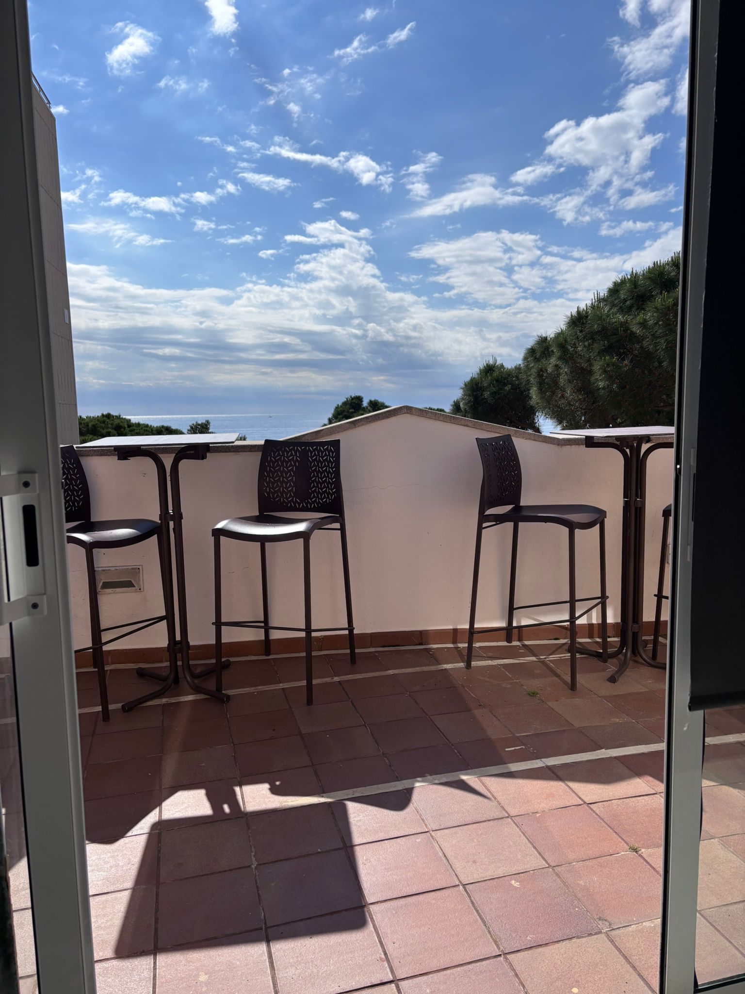 Balcón con patio, tres taburetes altos y vistas al cielo azul y las nubes