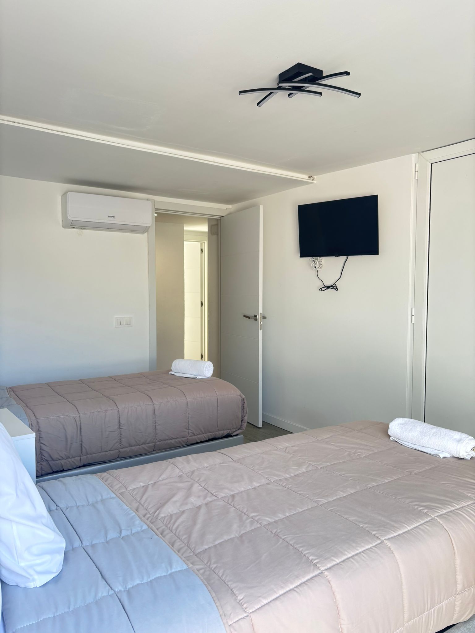 Dos camas individuales en una habitación de hotel luminosa y moderna, con televisor y aire acondicionado montados en la pared