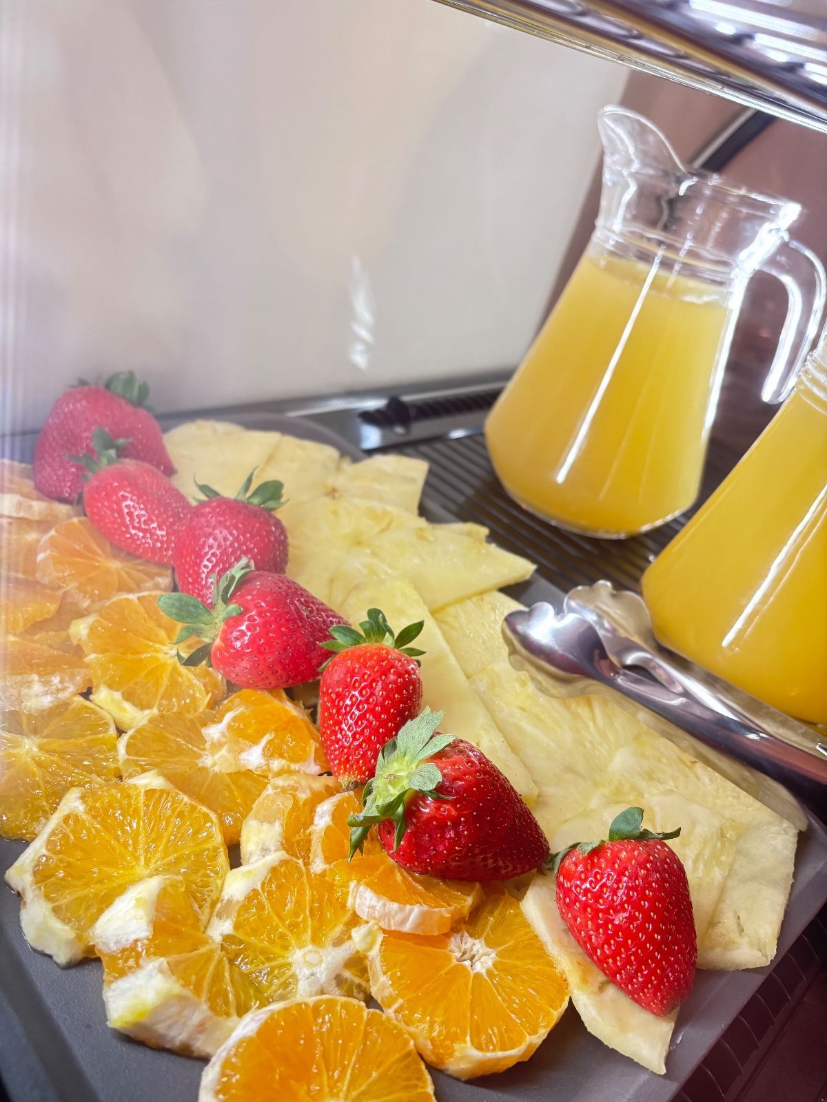 Bandeja de frutas con fresas y rodajas de naranja junto a una jarra de zumo de naranja sobre una mesa
