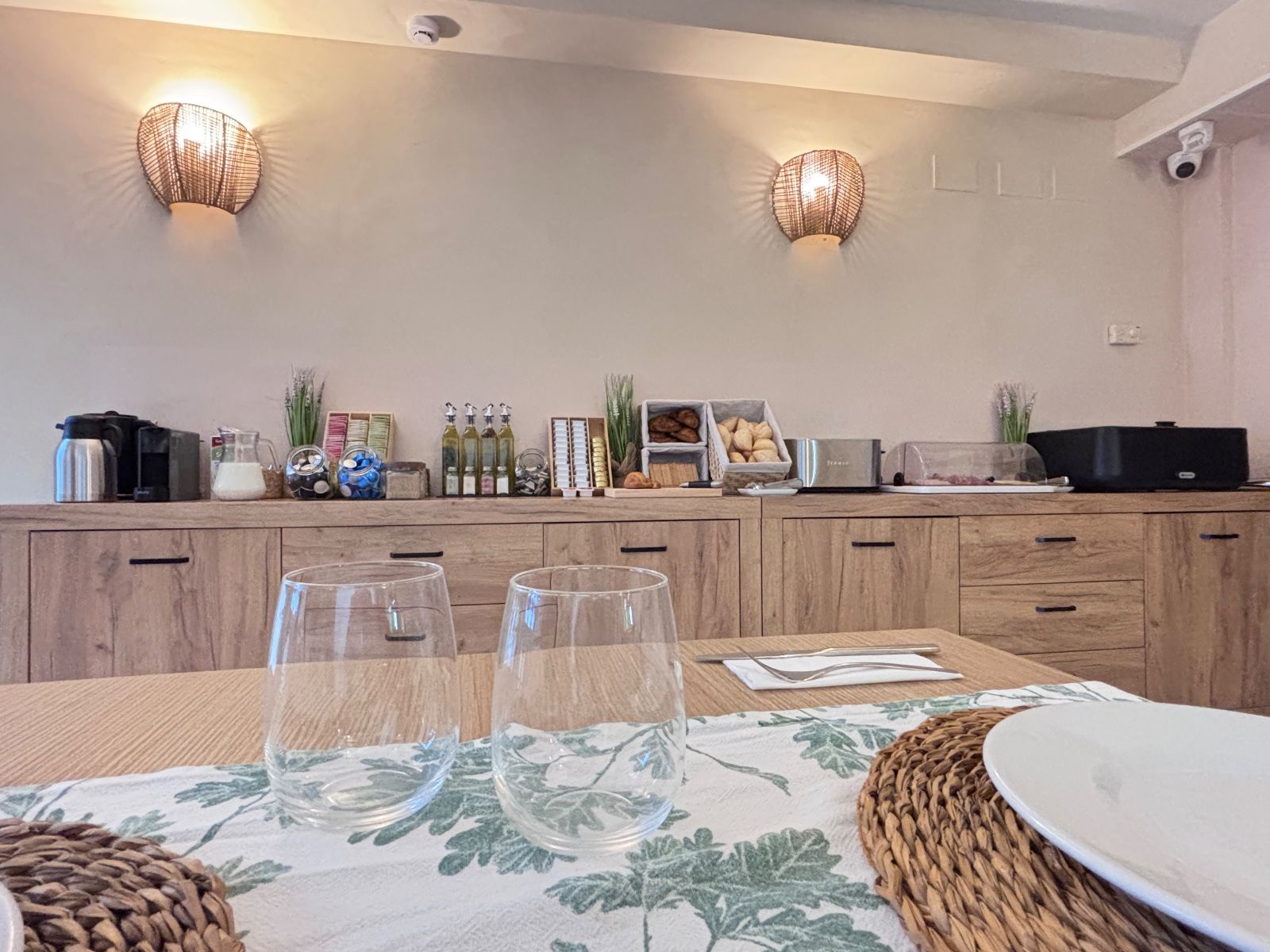 Comedor con aparador de madera, apliques de pared colgantes, mesa puesta y un mantel individual de fibras trenzadas.