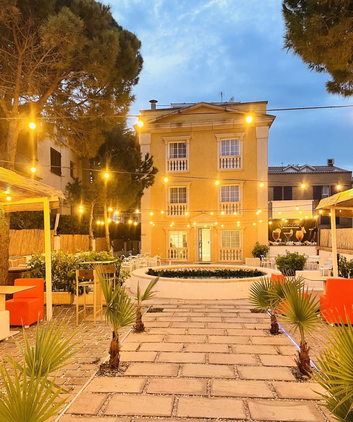 Patio iluminado con un camino de piedra, asientos naranjas y un edificio amarillo iluminado al atardecer