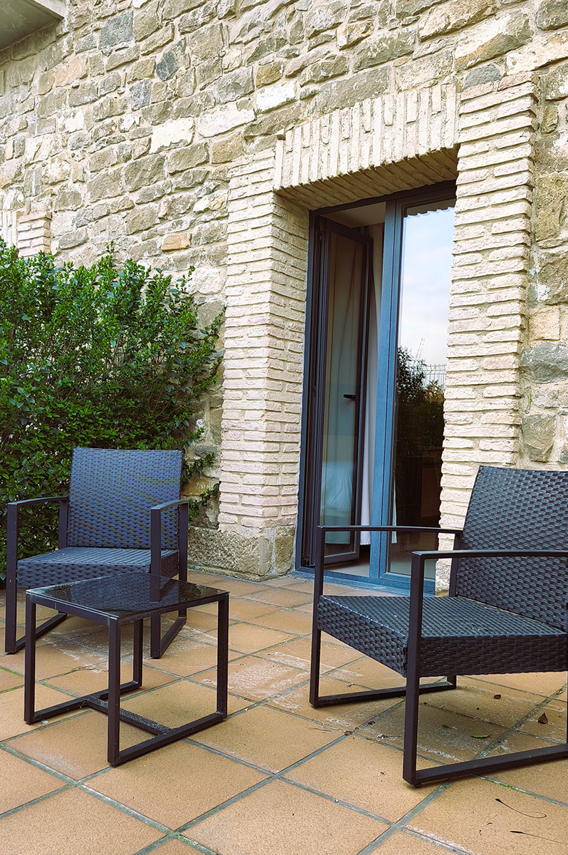 Two black patio chairs on a tiled terrace beside a stone wall and open doorway