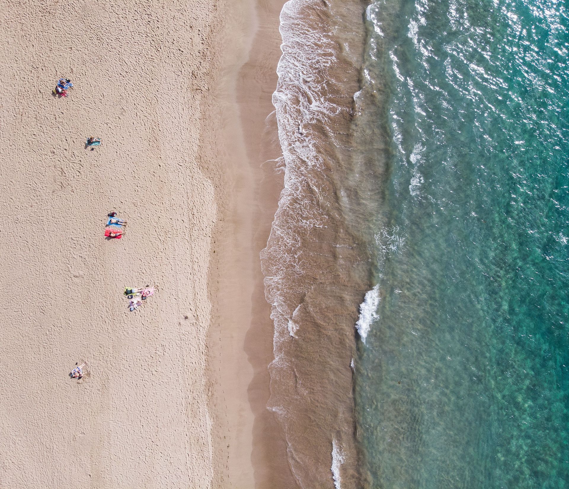 Gente nadando en una cala de aguas cristalinas de color turquesa, junto a acantilados rocosos y una playa de arena.