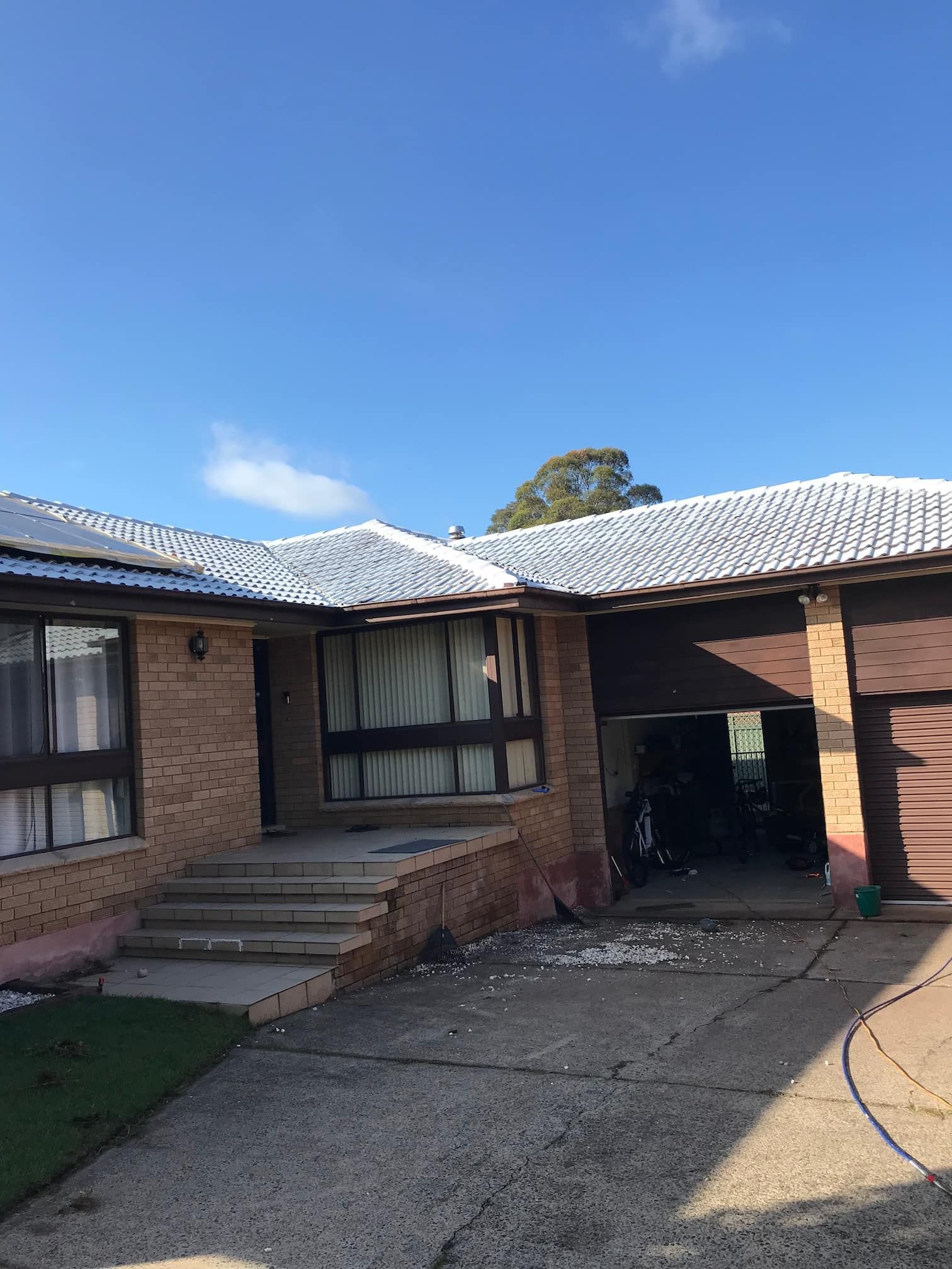 Brick house with white roof, front steps, and carport under a clear blue sky