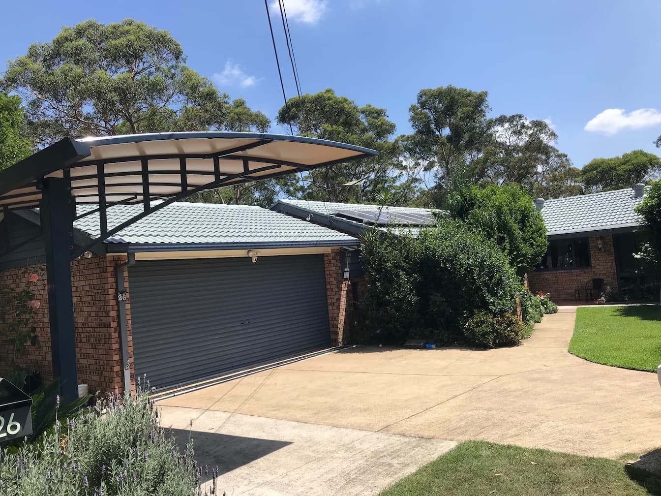 A house with a brick exterior, a grey tiled roof, a large garage, and a cantilevered shade structure over the driveway.