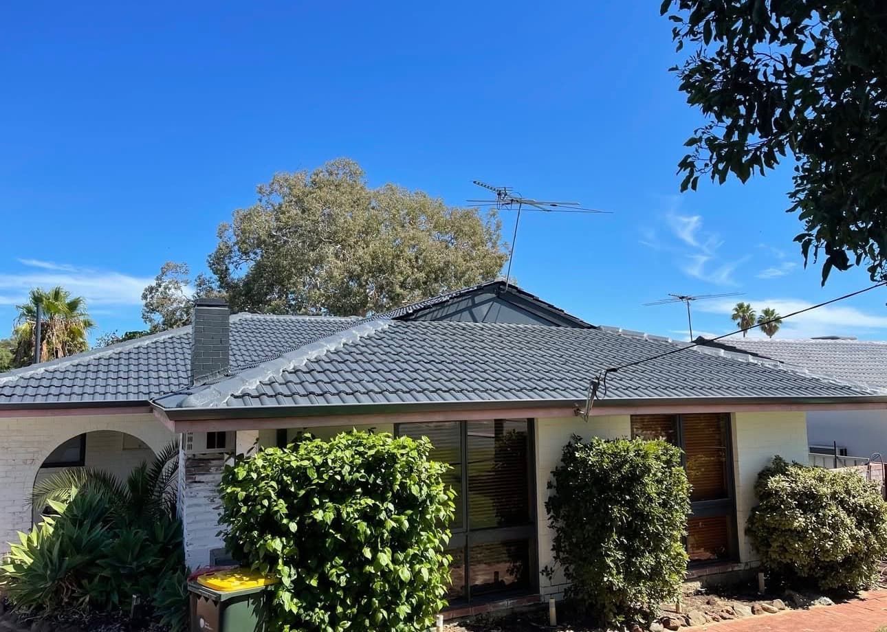 Single-story suburban house with a dark tiled roof, white walls, and front garden under a blue sky