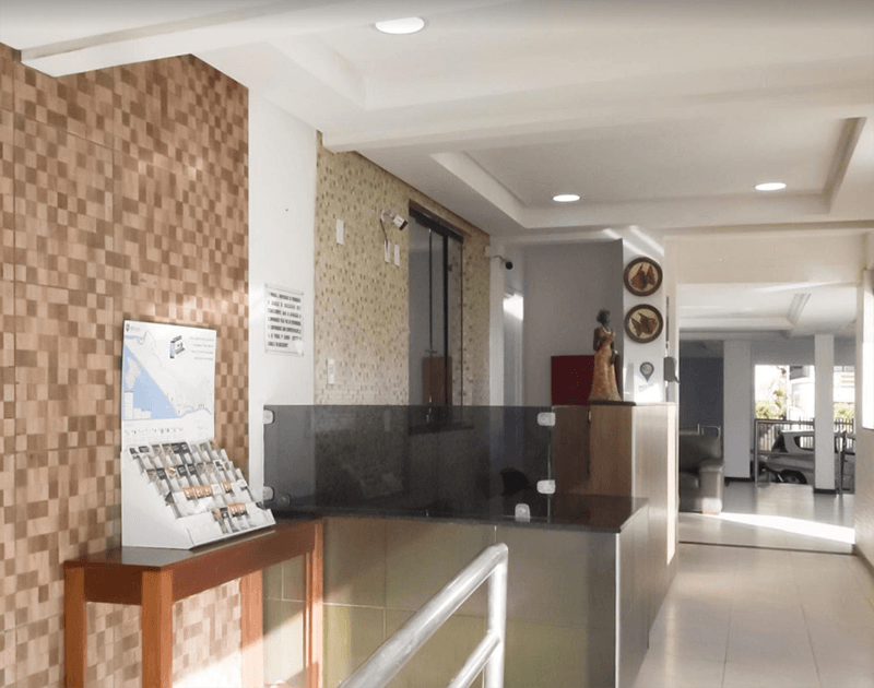 Hall de entrada do hotel com balcão de recepção, parede de tijolos decorativa e expositor de folhetos.
