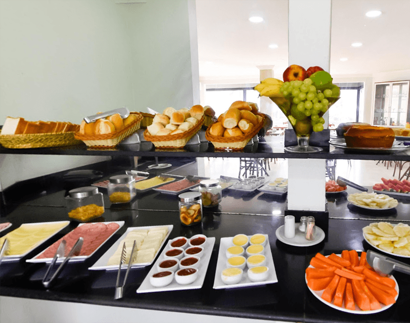 Buffet de café da manhã com pão, frutas, queijos, frios, geleias e ovos recheados.