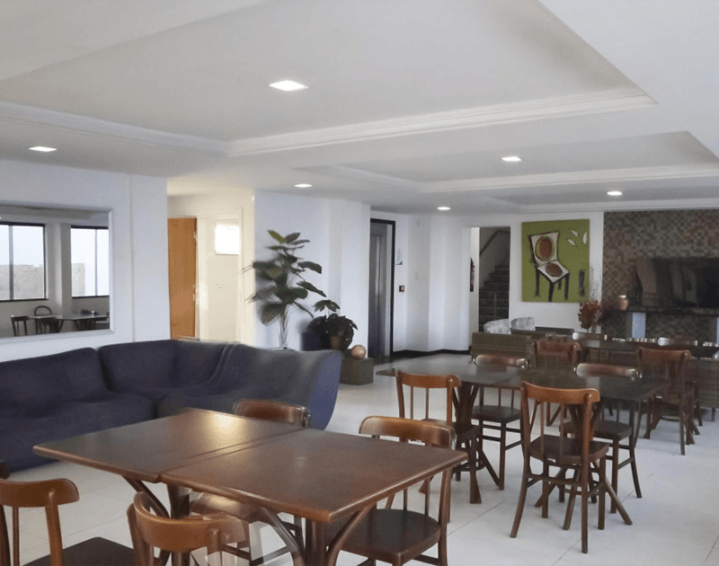 Interior de um café bem iluminado com mesas e cadeiras, um sofá grande e obras de arte nas paredes.