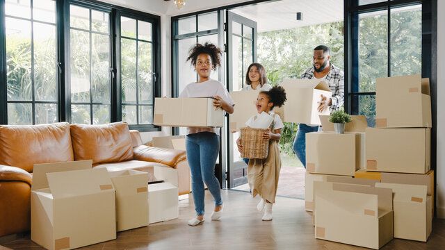 A family carries cardboard boxes into a bright, modern living room while moving into a new home.