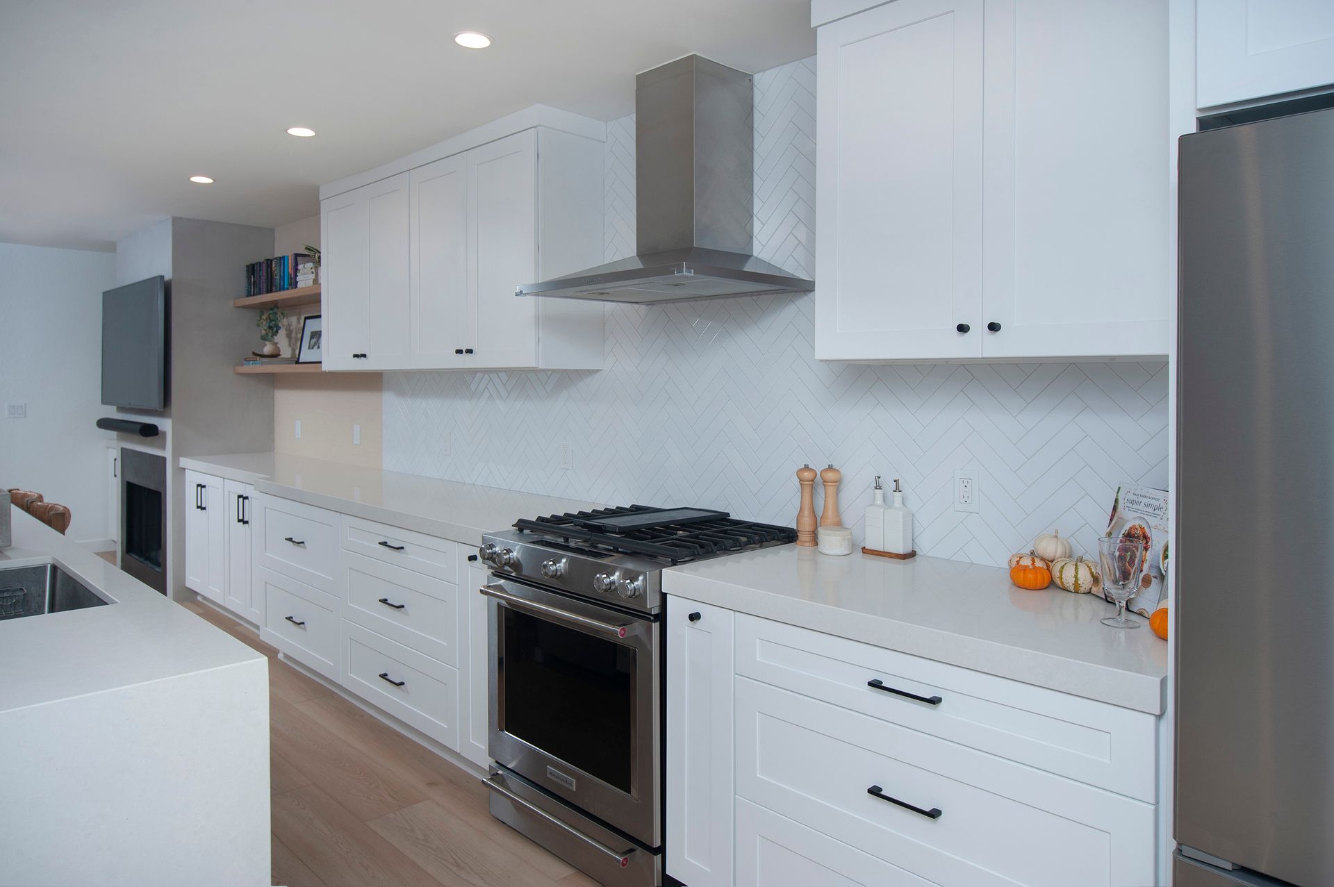 Modern white kitchen with stainless steel appliances, gas range, and light wood floors.
