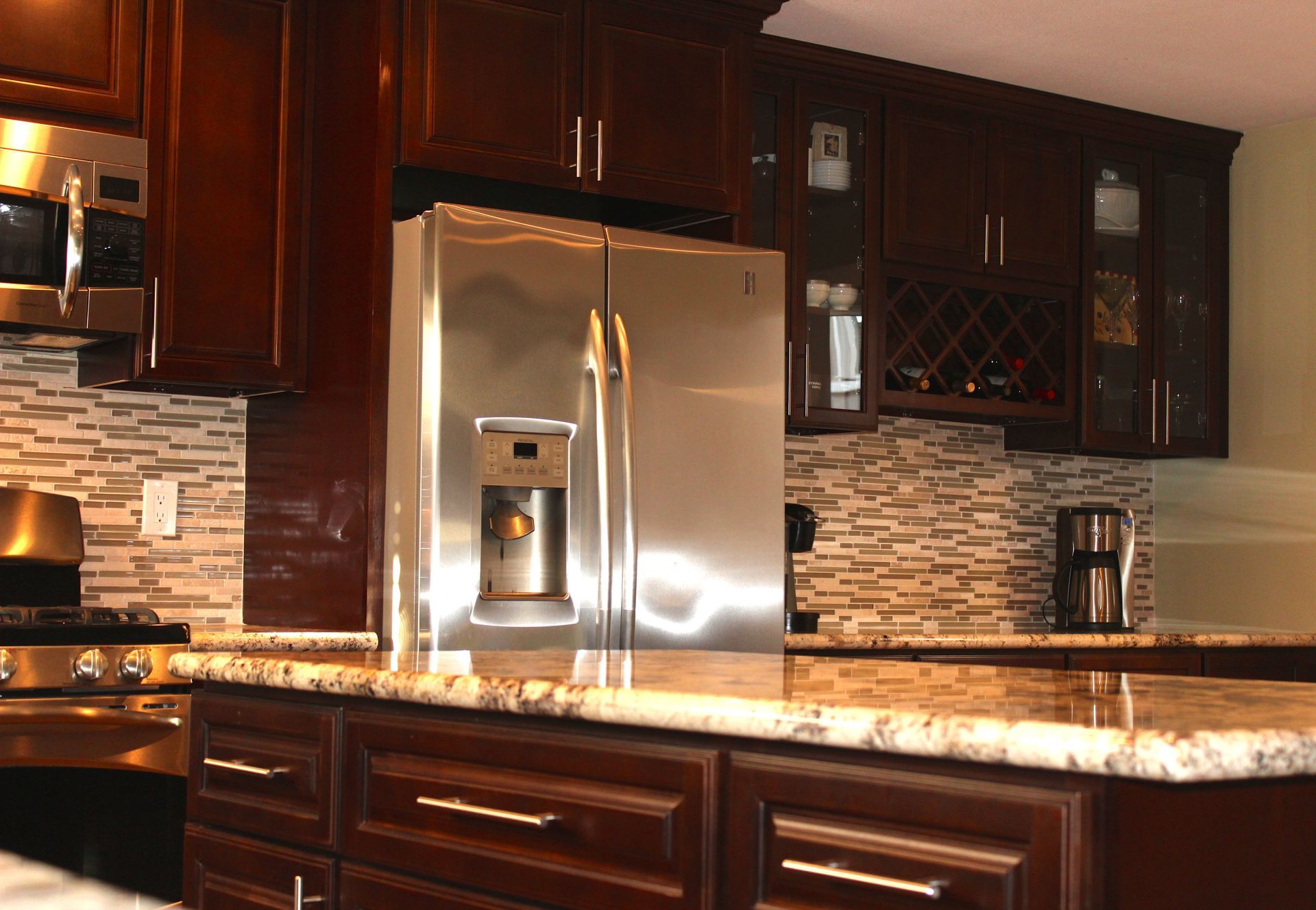 Kitchen with dark wood cabinets, stainless steel refrigerator, granite countertops, and mosaic tile backsplash.