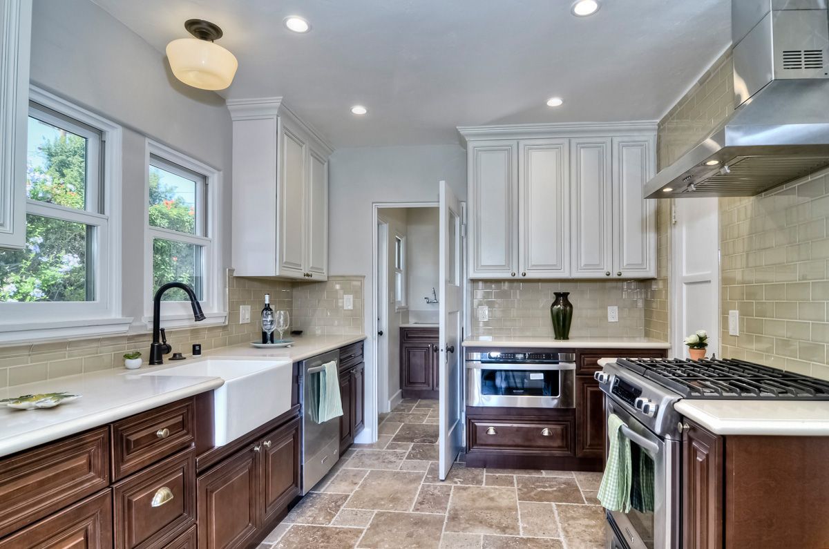 A kitchen with white upper cabinets, brown lower cabinets, and a farmhouse sink.