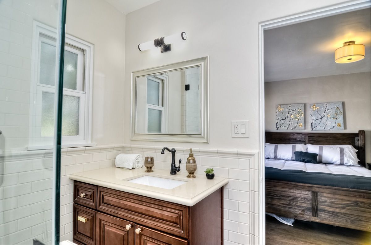 Bathroom with a vanity and a doorway to a bedroom. Brown vanity, white walls, and a large mirror.
