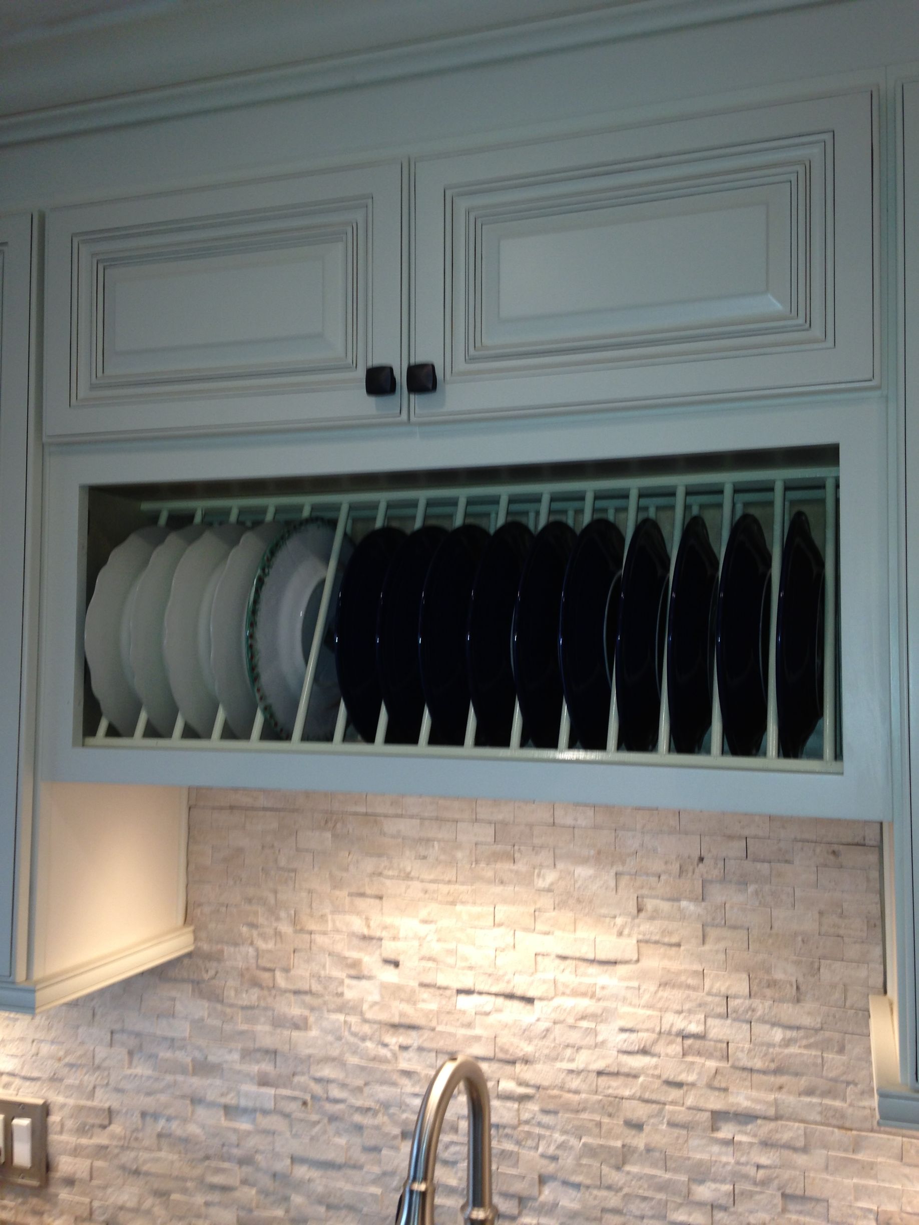 White plates in a built-in dish rack under white kitchen cabinets, above a tiled backsplash.