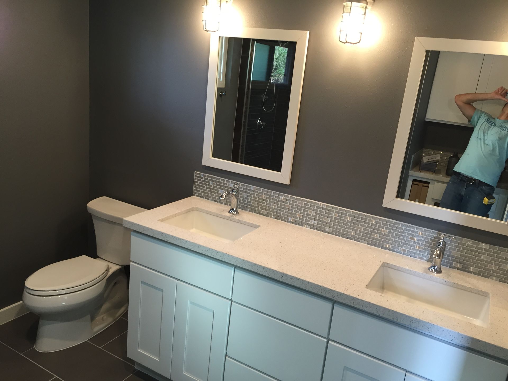 Bathroom with white vanity, two mirrors, gray walls and floor, and a toilet.