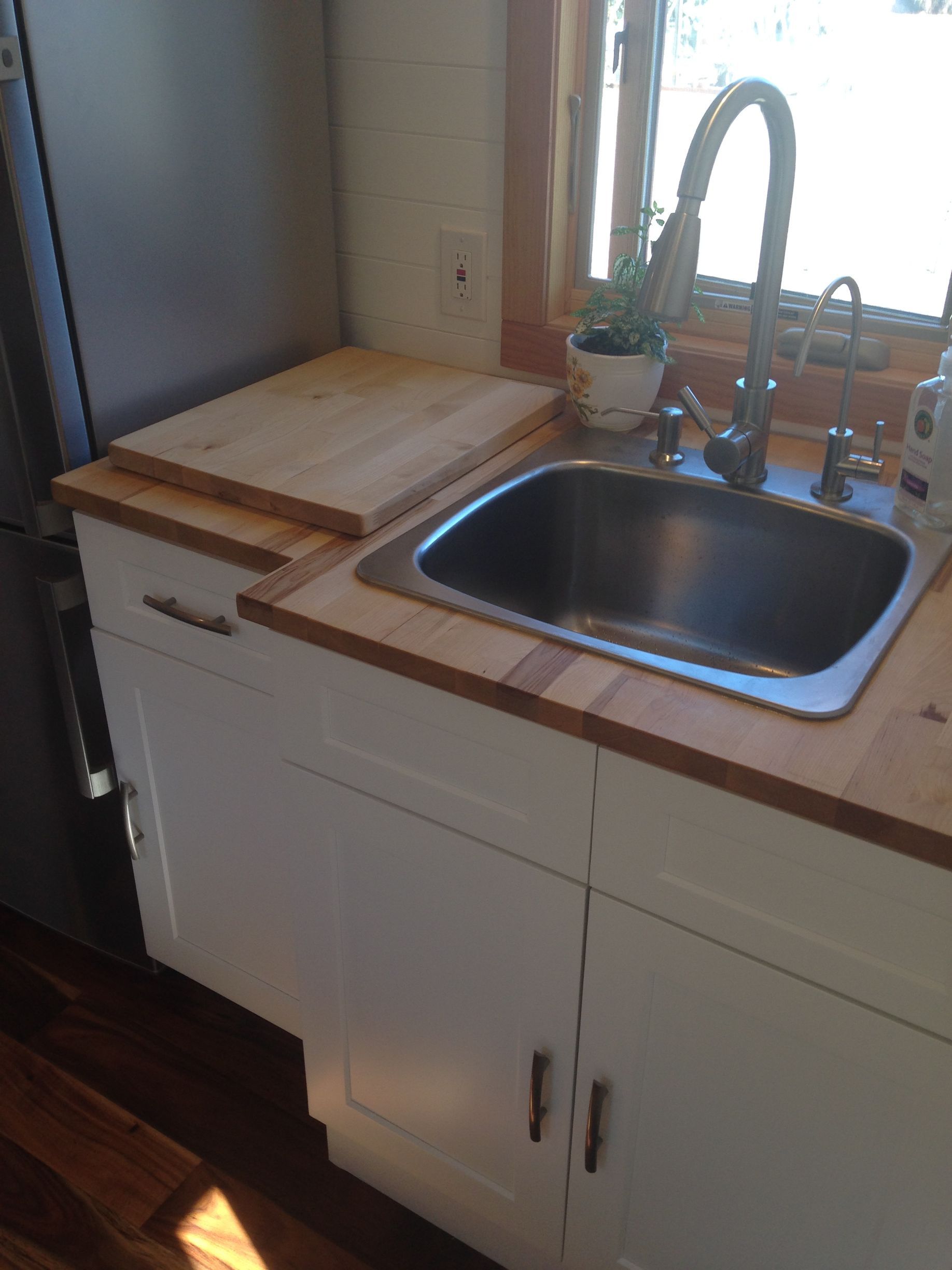 White kitchen cabinets with a stainless steel sink, wood countertop, and a cutting board.