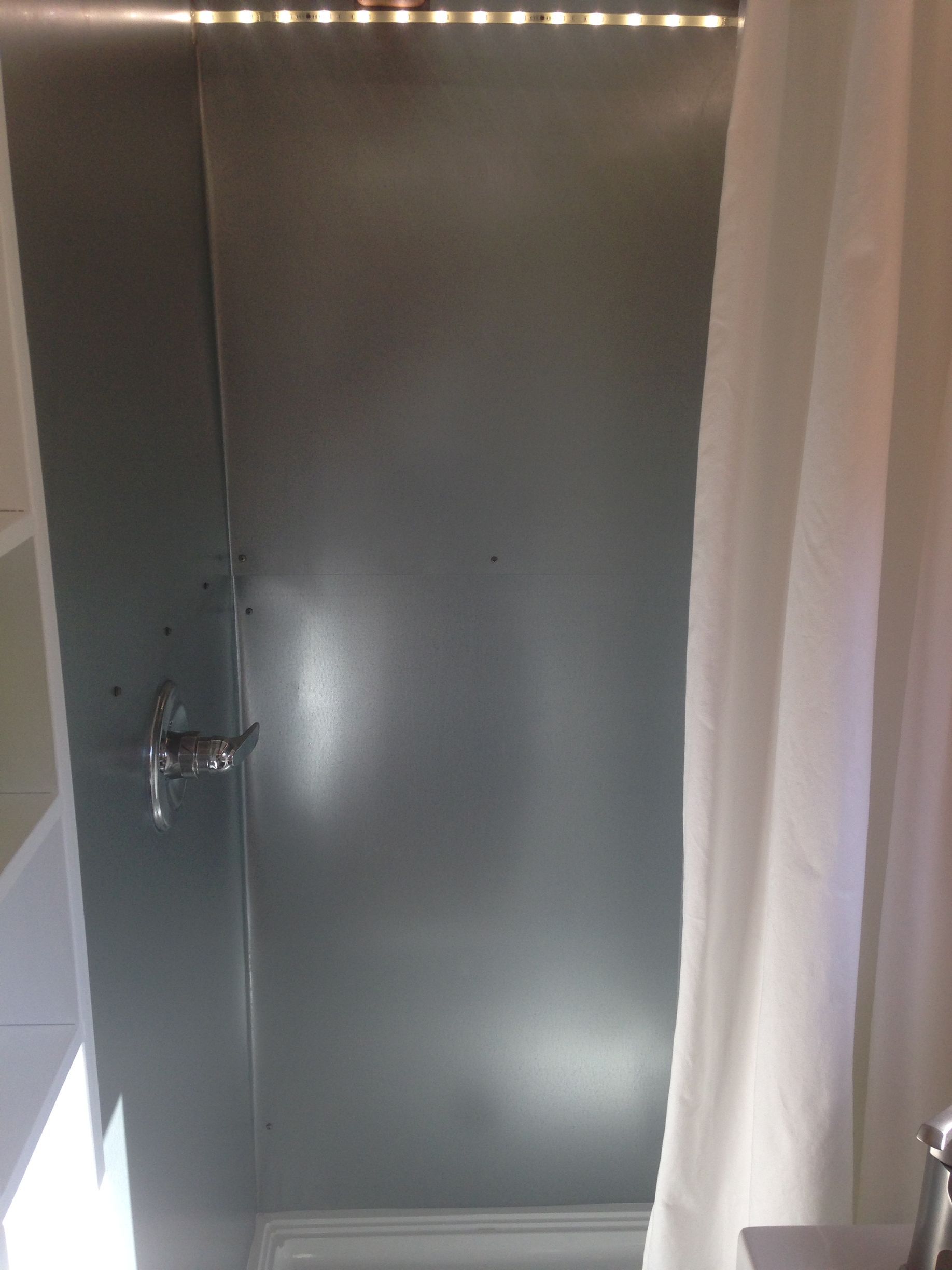 Shower with gray paneling, white curtain, and silver faucet. LED lights above.