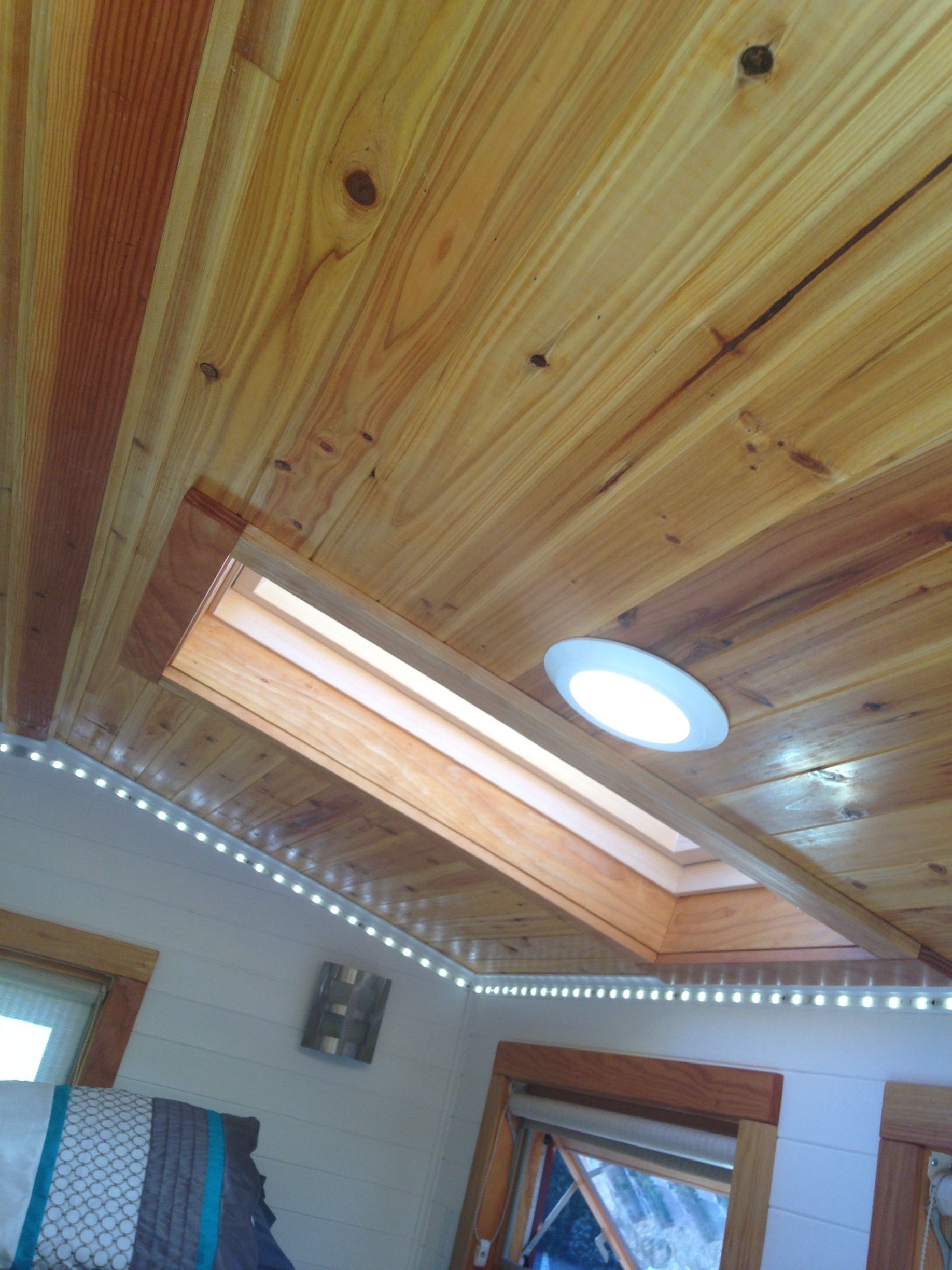 Wooden ceiling with skylight and LED strip lights, inside a cabin.