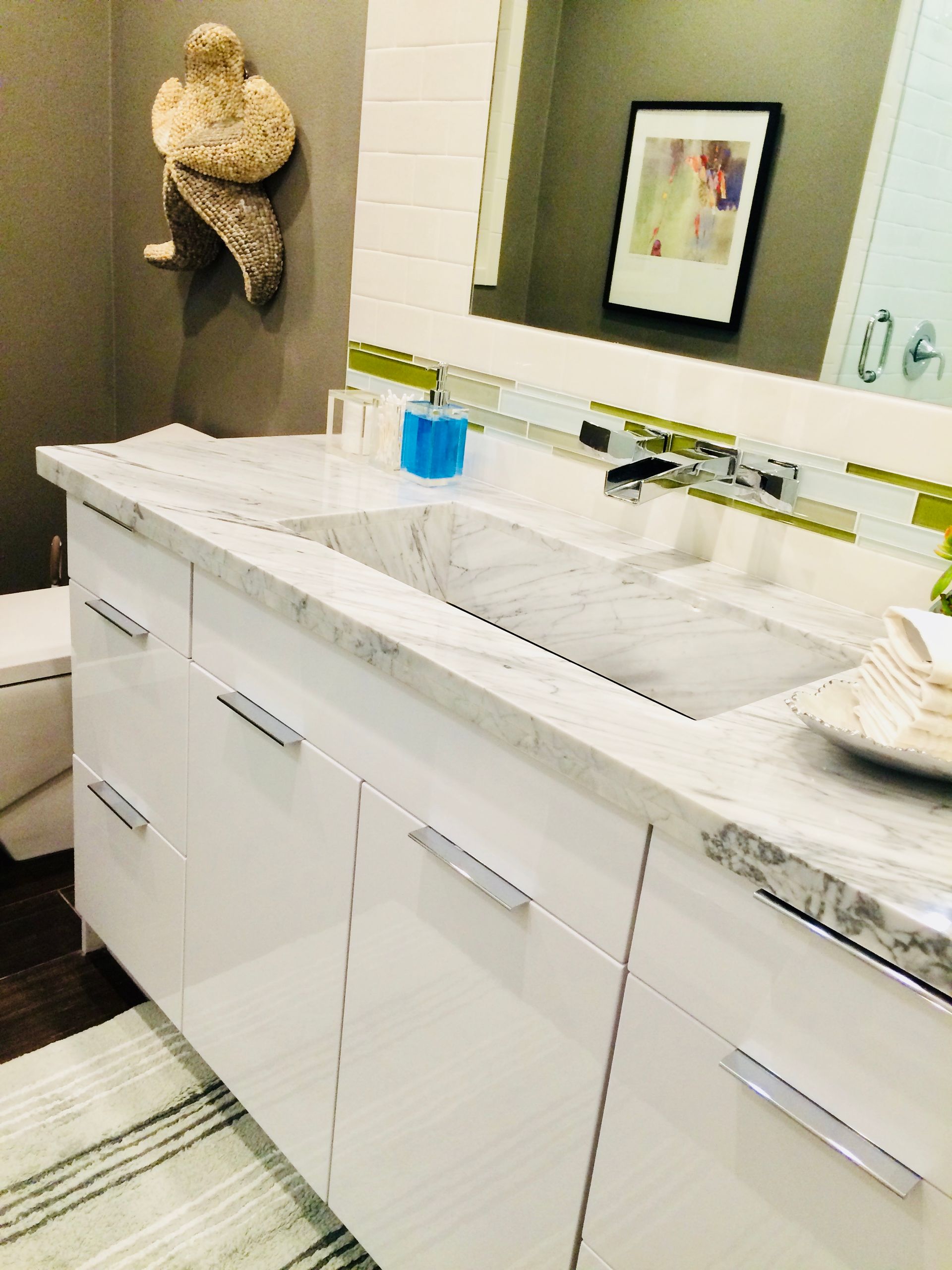 White bathroom vanity with marble countertop, green accents, and art.