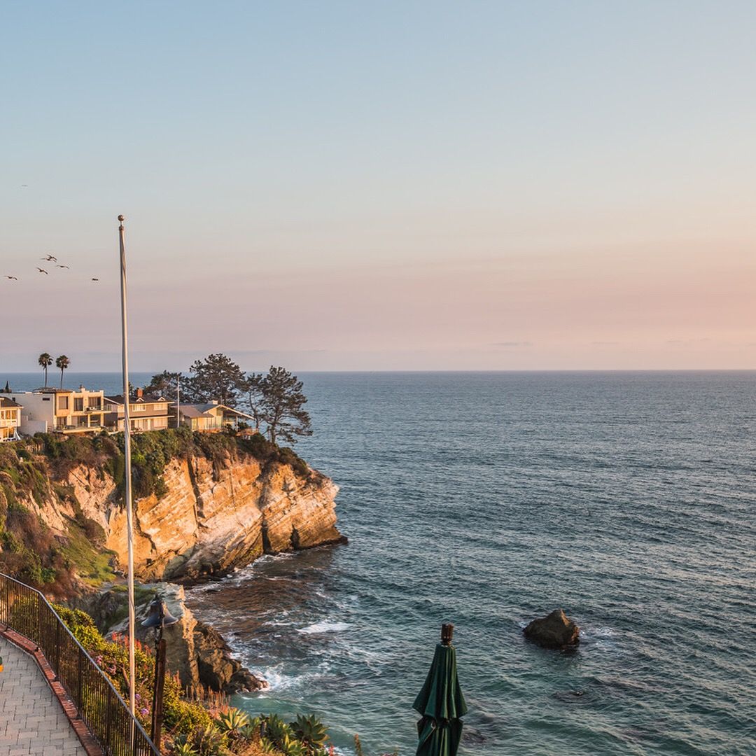 Coastal view with cliffs, ocean, buildings, and a sunset sky.