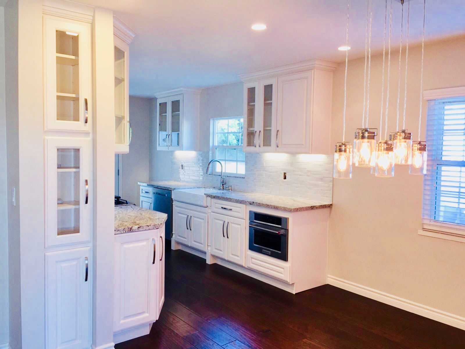 White kitchen with cabinets, marble backsplash, dark wood floors, and a modern light fixture.