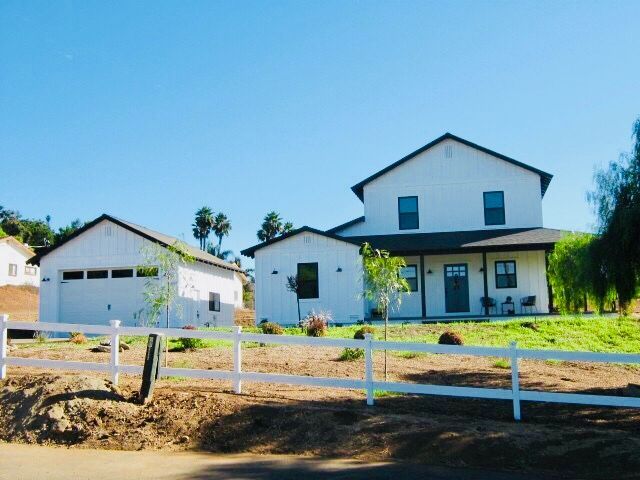 White farmhouse and detached garage with a white fence under a blue sky.