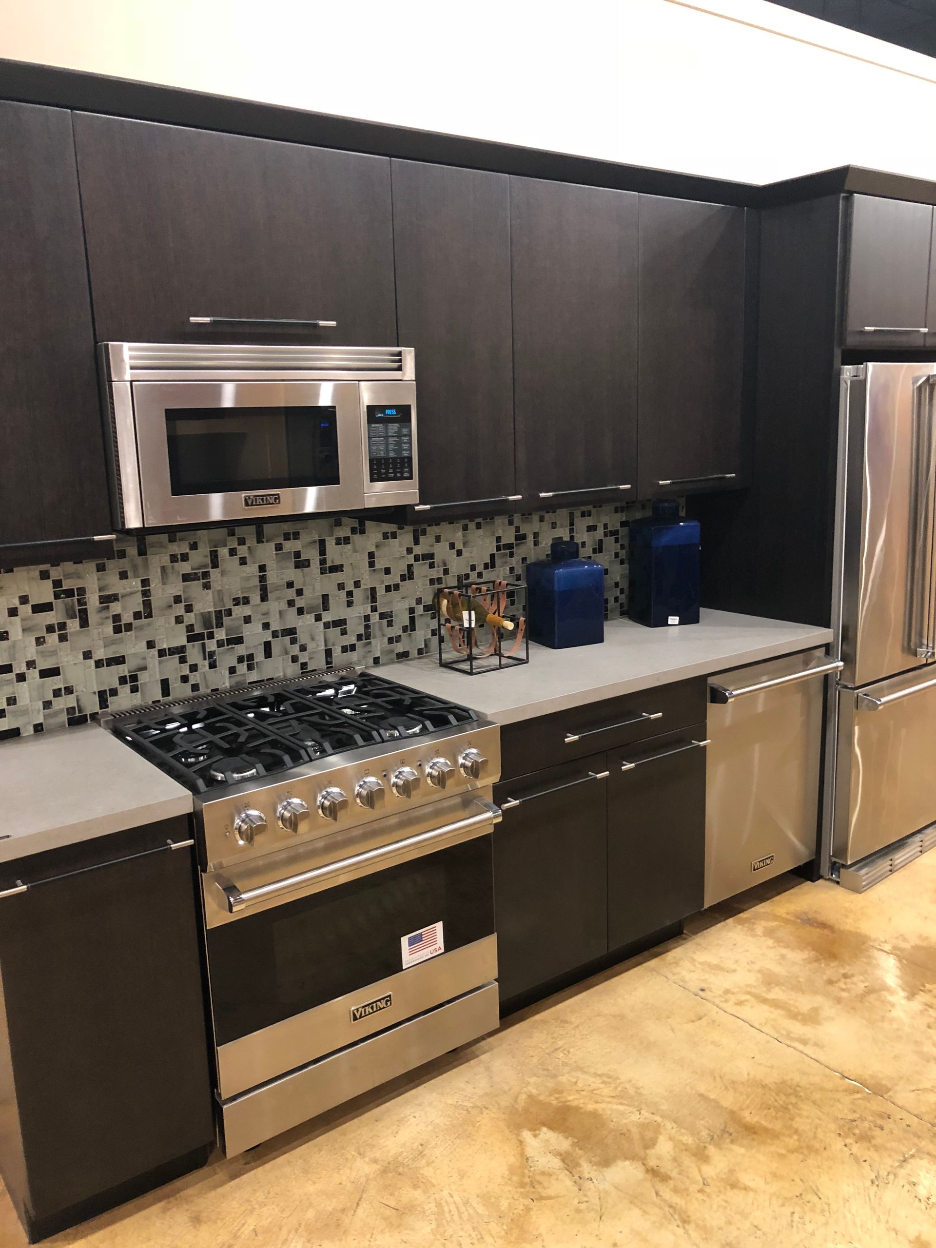 Modern kitchen with dark cabinets, stainless steel appliances, and mosaic tile backsplash.
