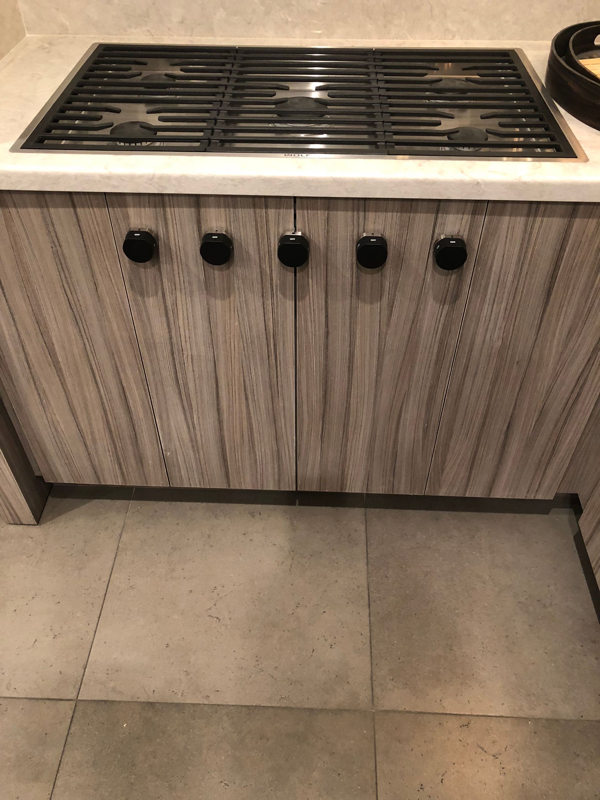 Gas stovetop with black knobs above wooden cabinet doors on tiled floor.