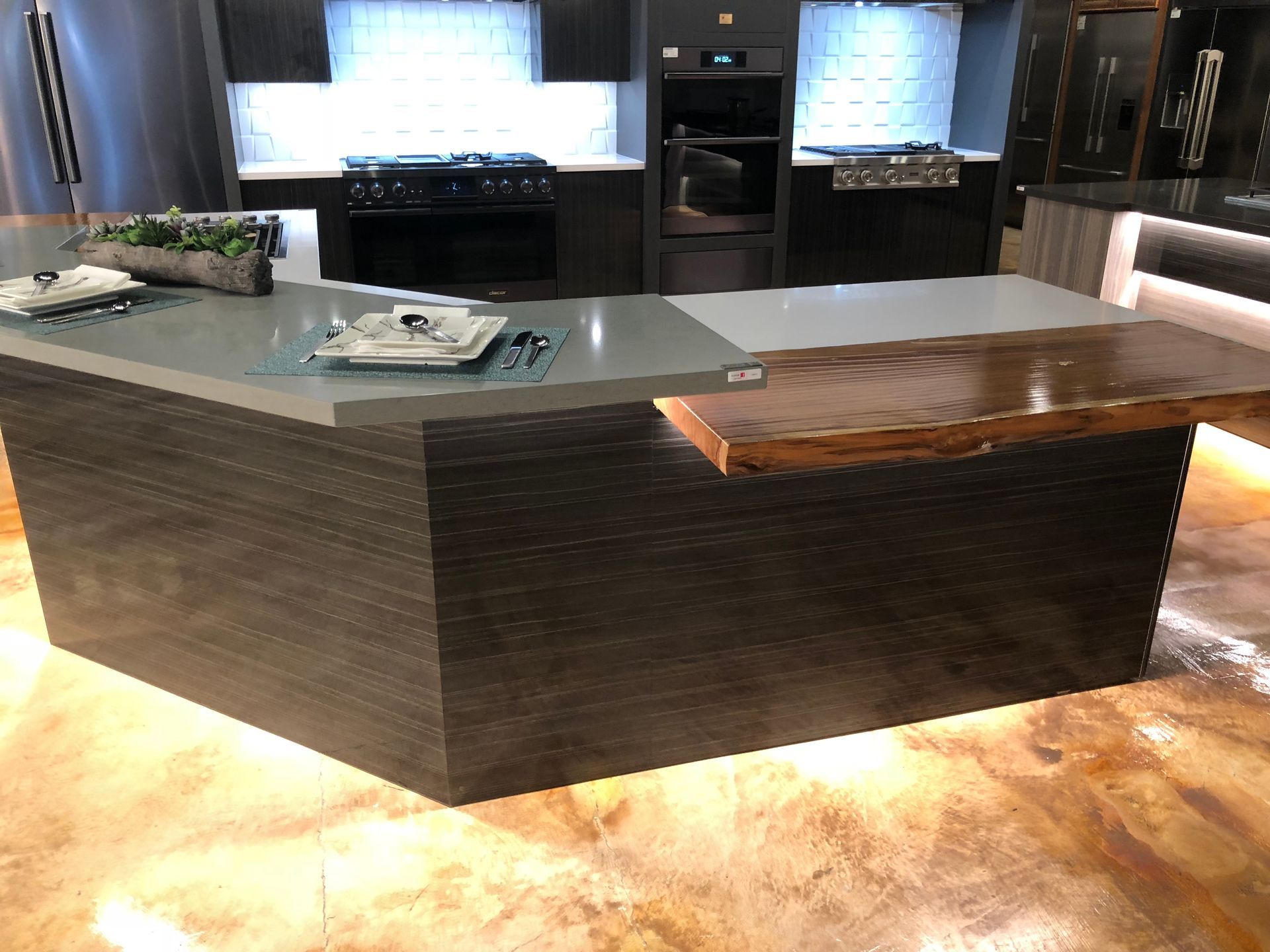 Modern kitchen island with gray countertop, dark wood cabinets, and a smaller wood overhang.