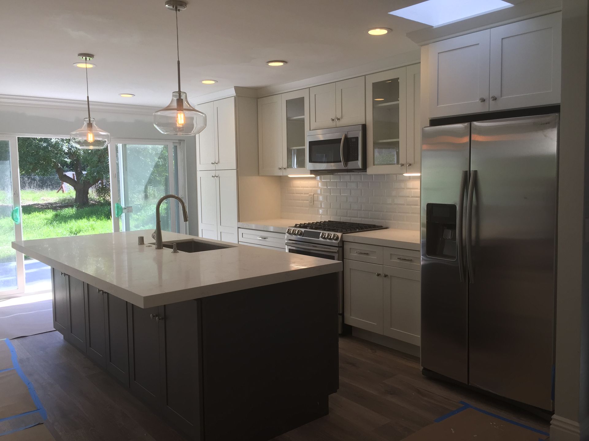 Modern kitchen with white and gray cabinets, stainless steel appliances, island with sink, and large windows.