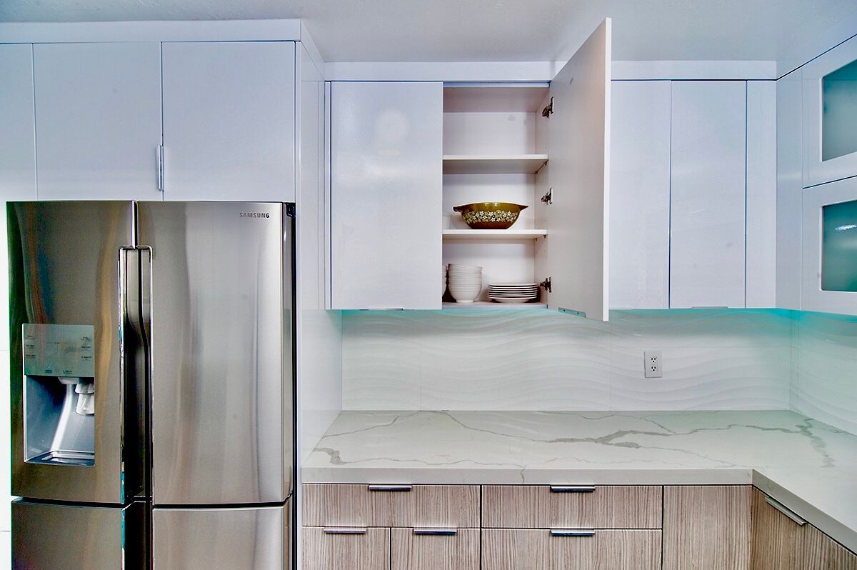 Stainless steel refrigerator next to white cabinets; one cabinet door open, revealing shelf with dishes.