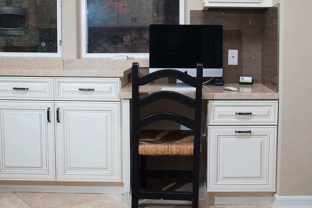 A computer is sitting on top of a desk in a kitchen.