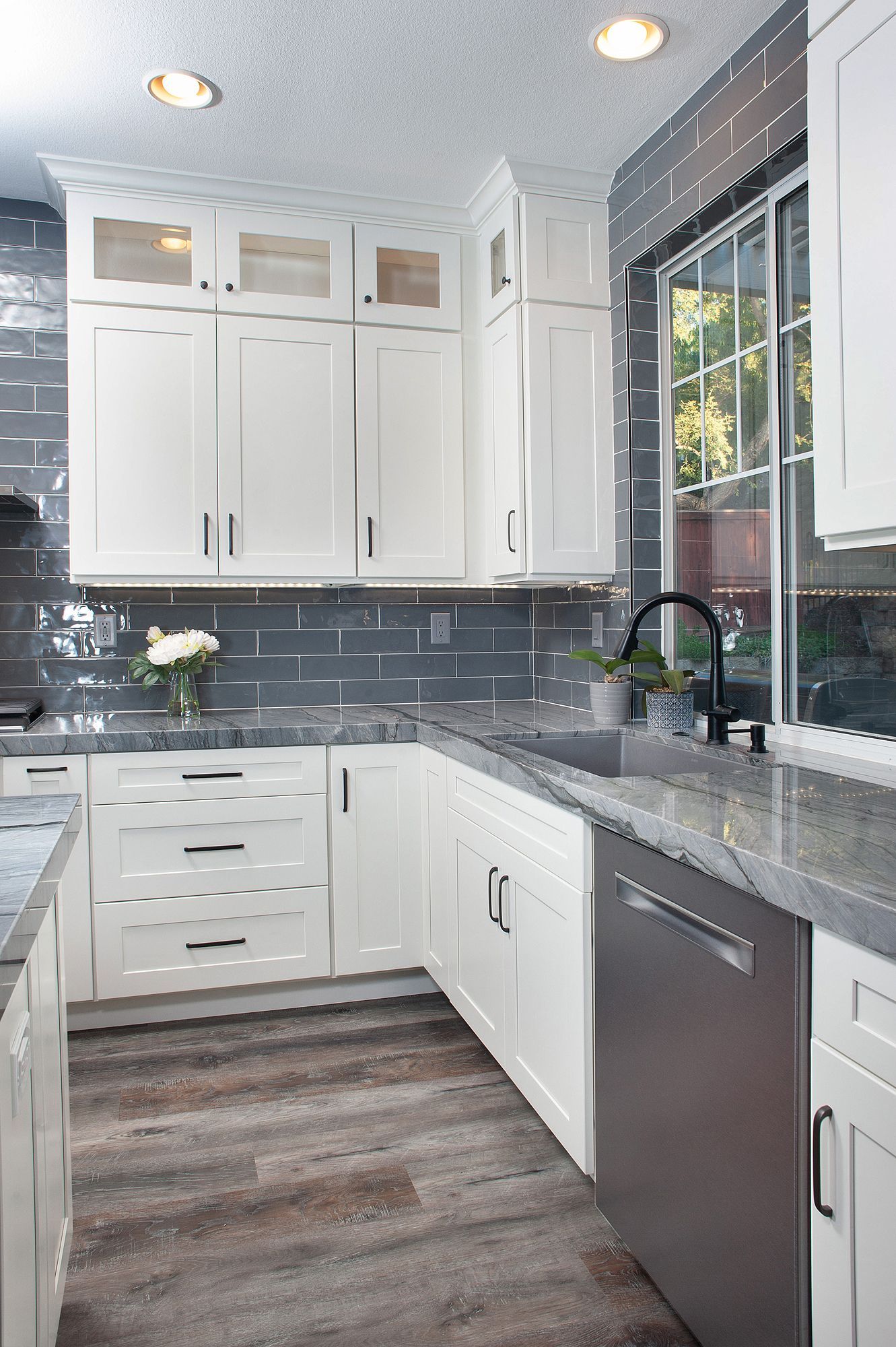 White kitchen with gray backsplash, stainless steel appliances, and wood-look floors.
