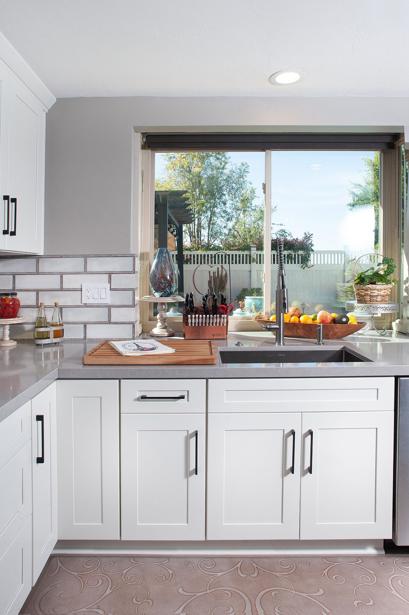 White kitchen with gray countertop, sink under window, stainless steel faucet and appliances.