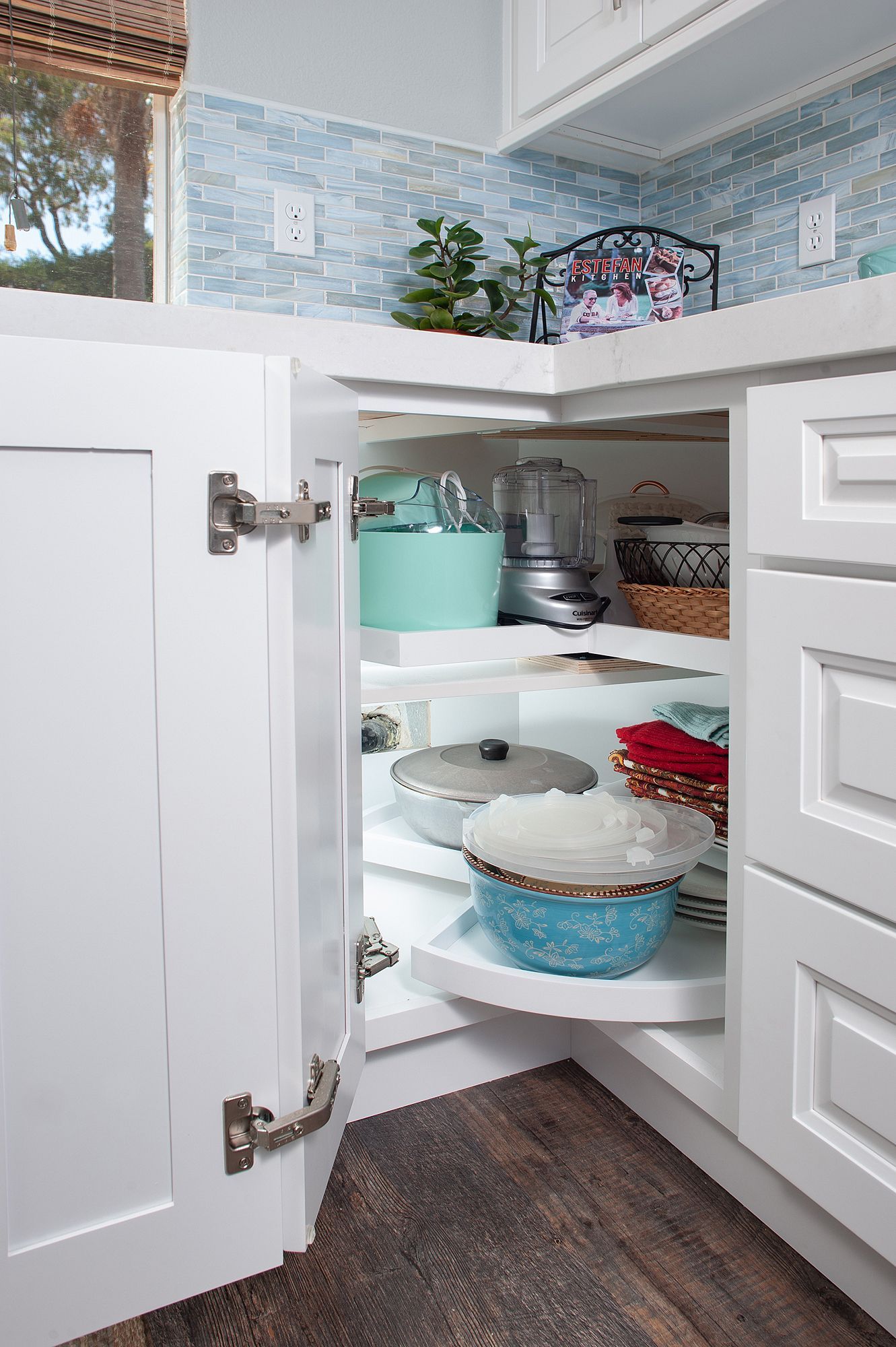 White corner kitchen cabinet with pull-out shelves holding dishes and appliances.