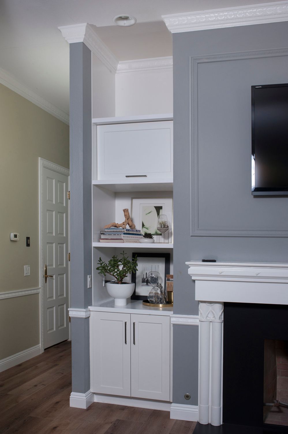 Built-in white cabinet with shelves between gray walls, a fireplace, and a TV on the right.