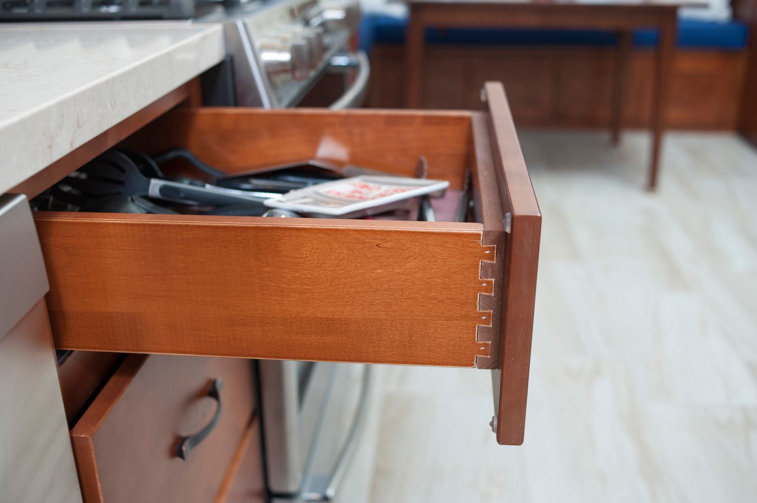 Open kitchen drawer with dovetail joints; brown wood, cluttered contents.