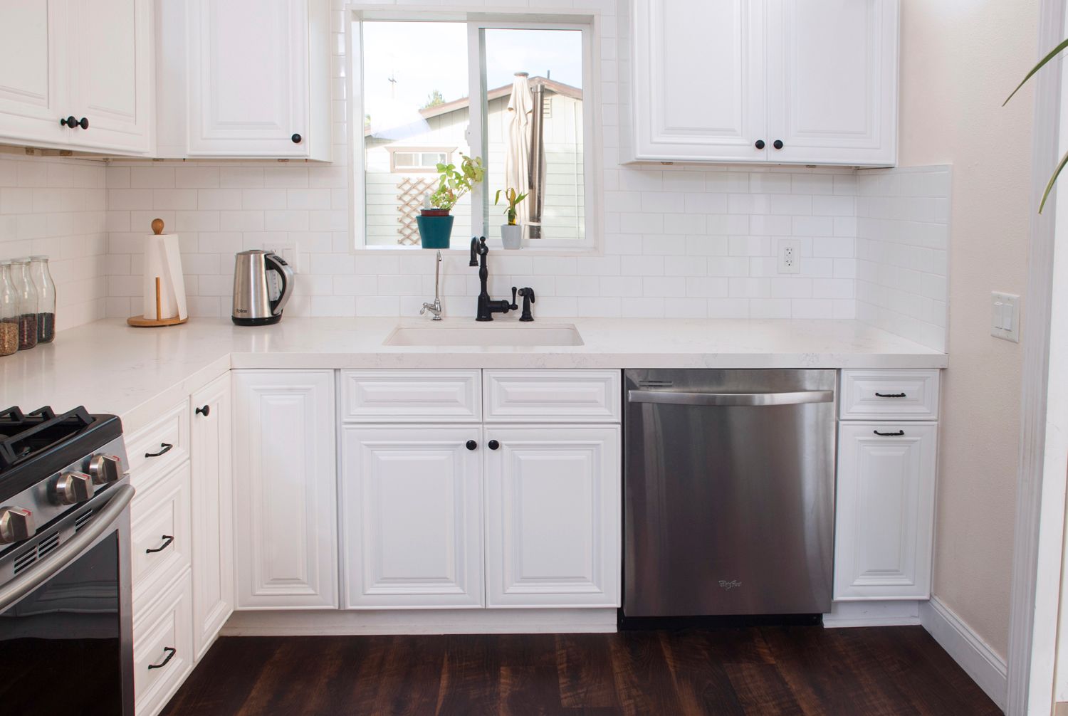 White kitchen with stainless steel appliances, dark wood floors, and window over the sink.