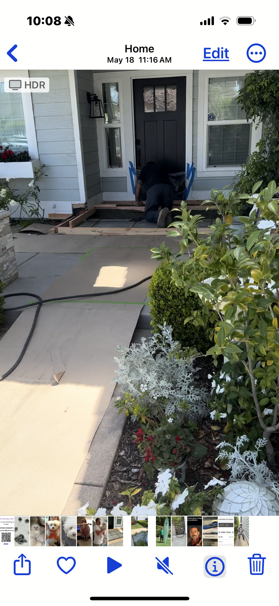 A person kneels near a home's door, possibly working on the entrance. Snow covers the nearby bushes and flowers.