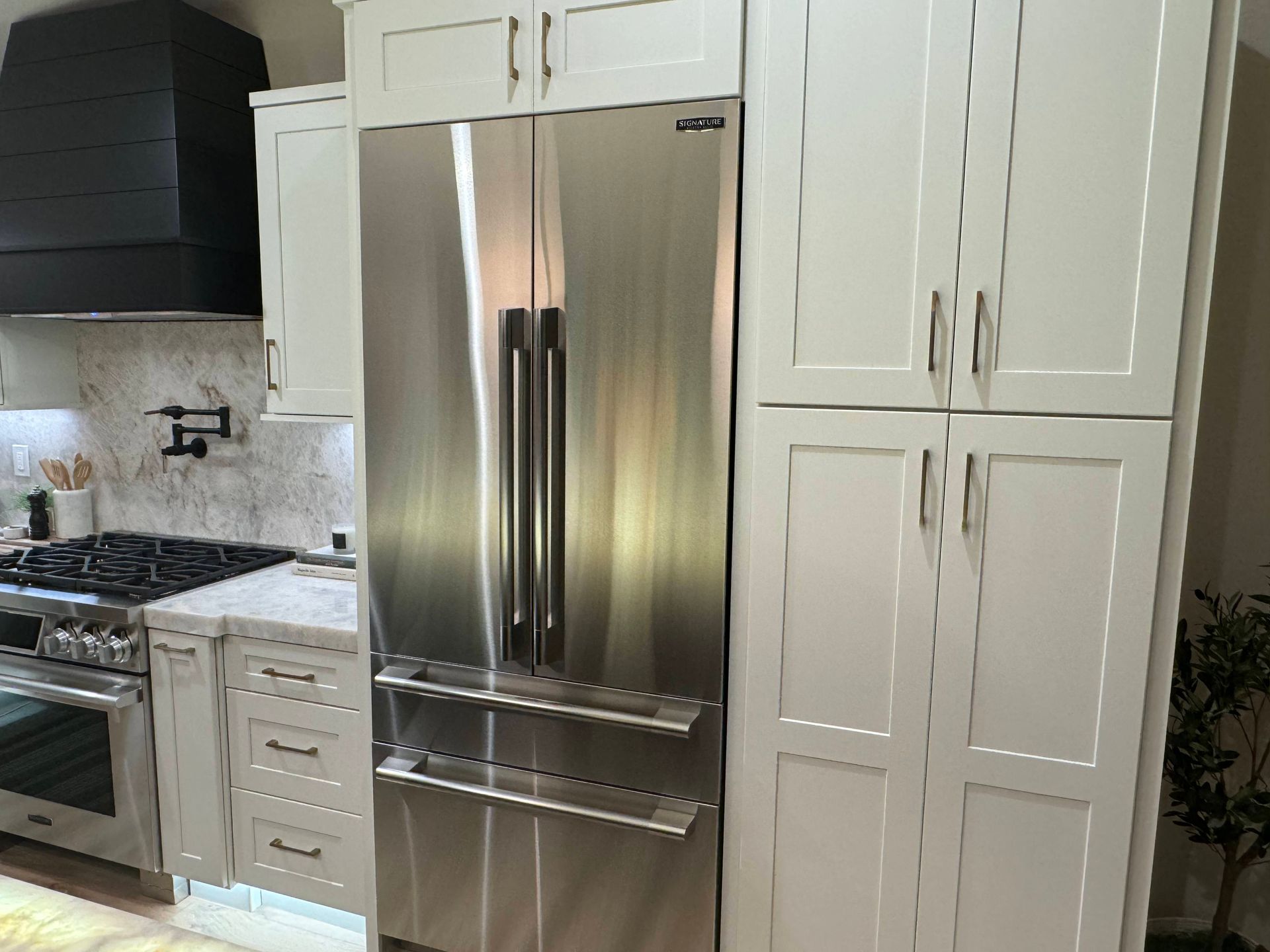 Stainless steel refrigerator in a kitchen with white cabinetry and a black range hood.