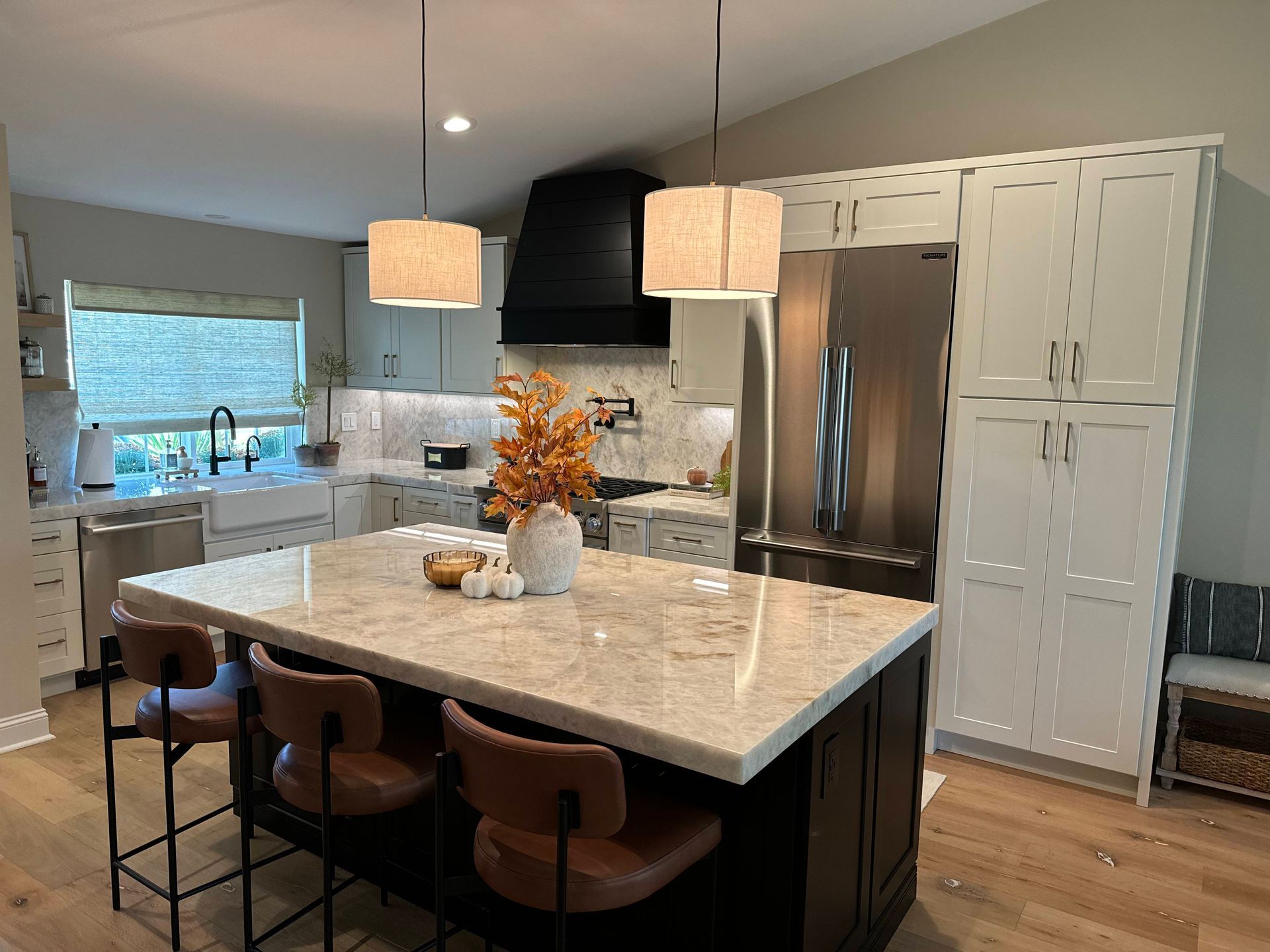 Modern kitchen with island, pendant lights, black range hood, and stainless steel refrigerator.