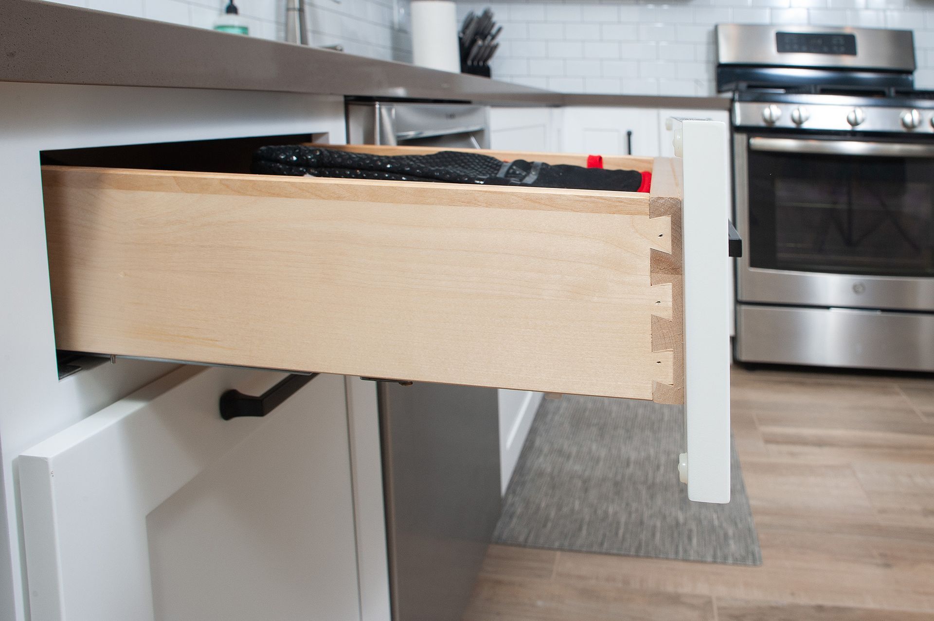Open kitchen drawer revealing contents, with stainless steel appliances in the background.
